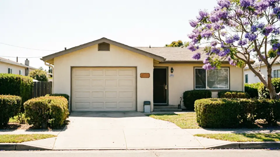 A beige house with a closed beige garage door and a purple flowering tree.